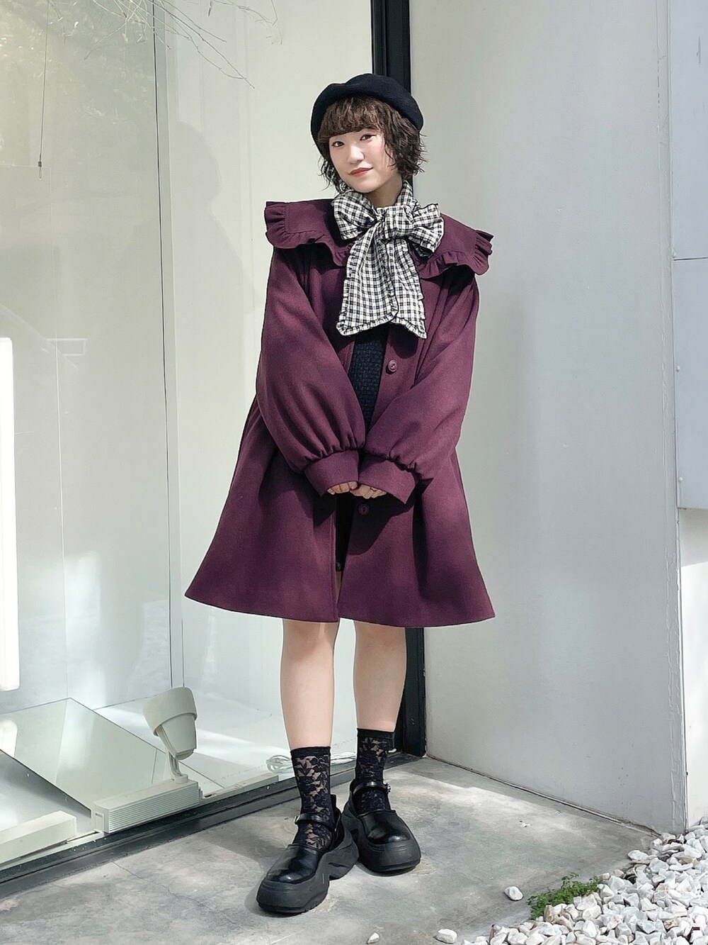 ブラック系のスニーカー、レッド系のチェスターコート、ブラック系のジャンパースカートを着用したレディースの秋コーディネートの2枚目の写真