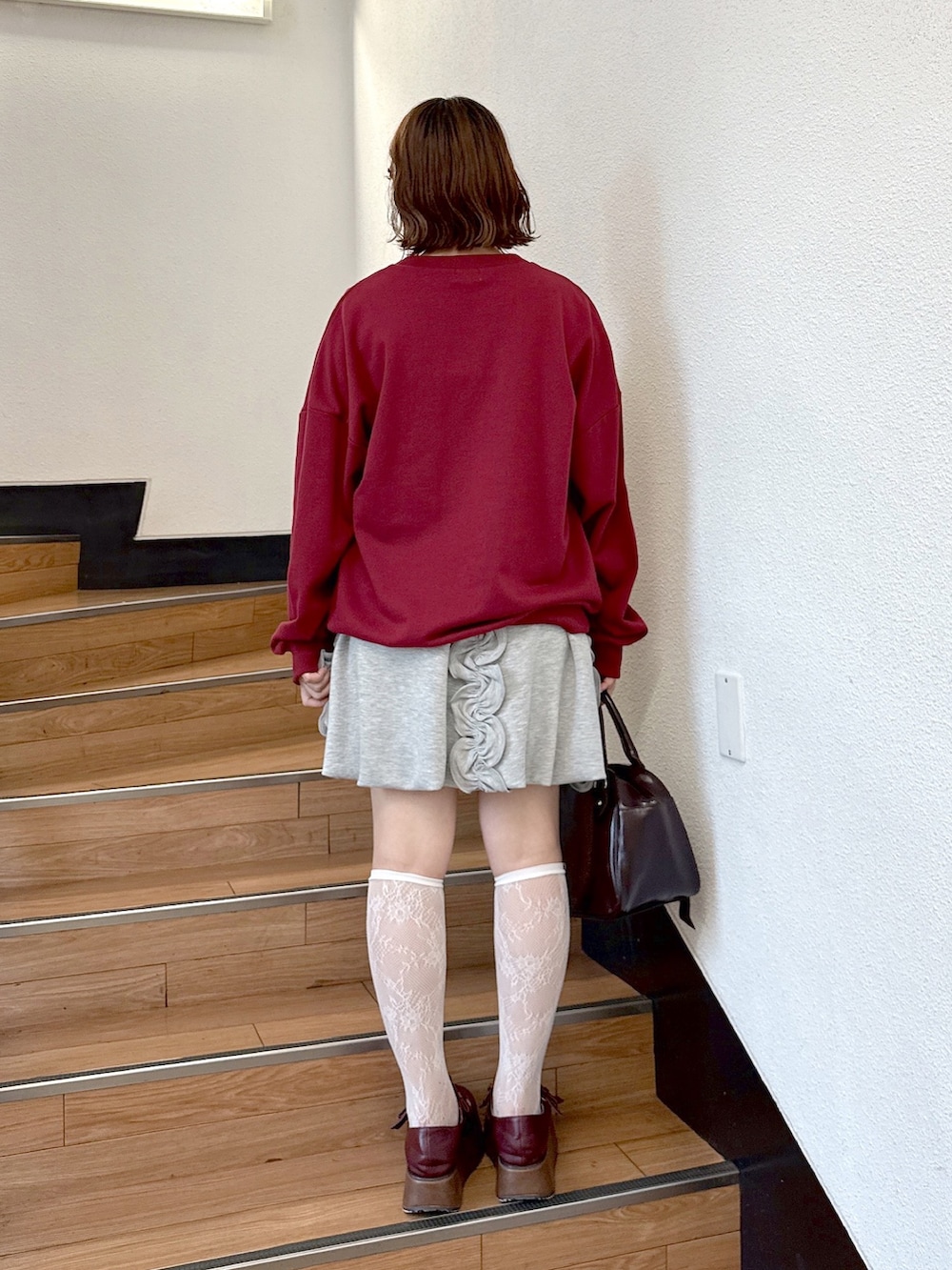 レッド系のスウェット、グレー系のスカート、ブラウン系のハンドバッグを着用したレディースの夏コーディネートの3枚目の写真