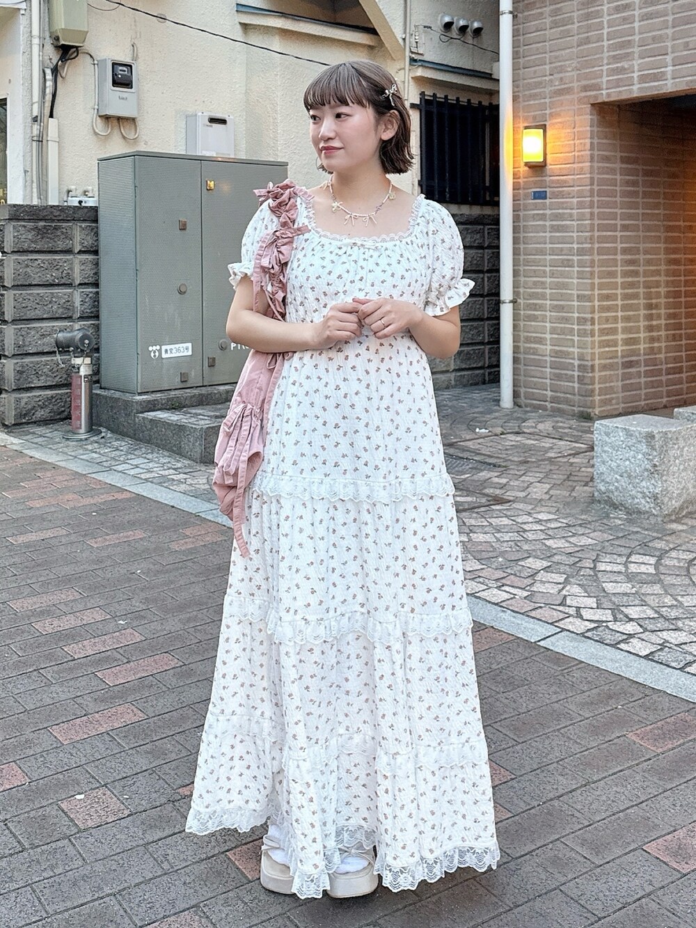 ピンク系のトートバッグ、ベージュ系のサンダル、ホワイト系のワンピースを着用したレディースの春コーディネートの2枚目の写真