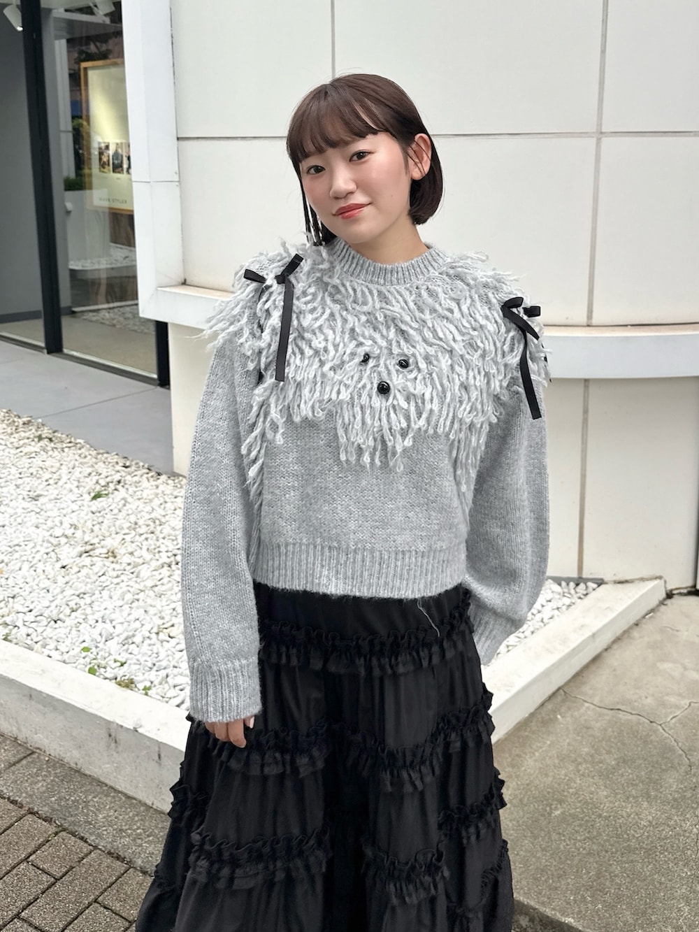 グレー系のニット/セーター、ブラック系のスカート、ブラック系のスニーカーを着用したレディースの夏コーディネートの4枚目の写真