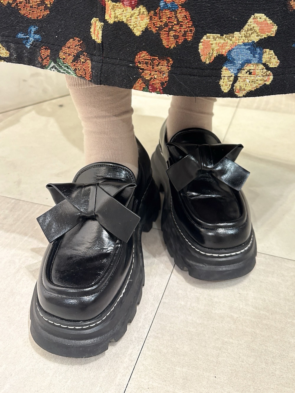 グレー系のニット/セーター、ブラック系のカーディガン/ボレロ、ブラック系のジャンパースカートを着用したレディースの秋コーディネートの7枚目の写真