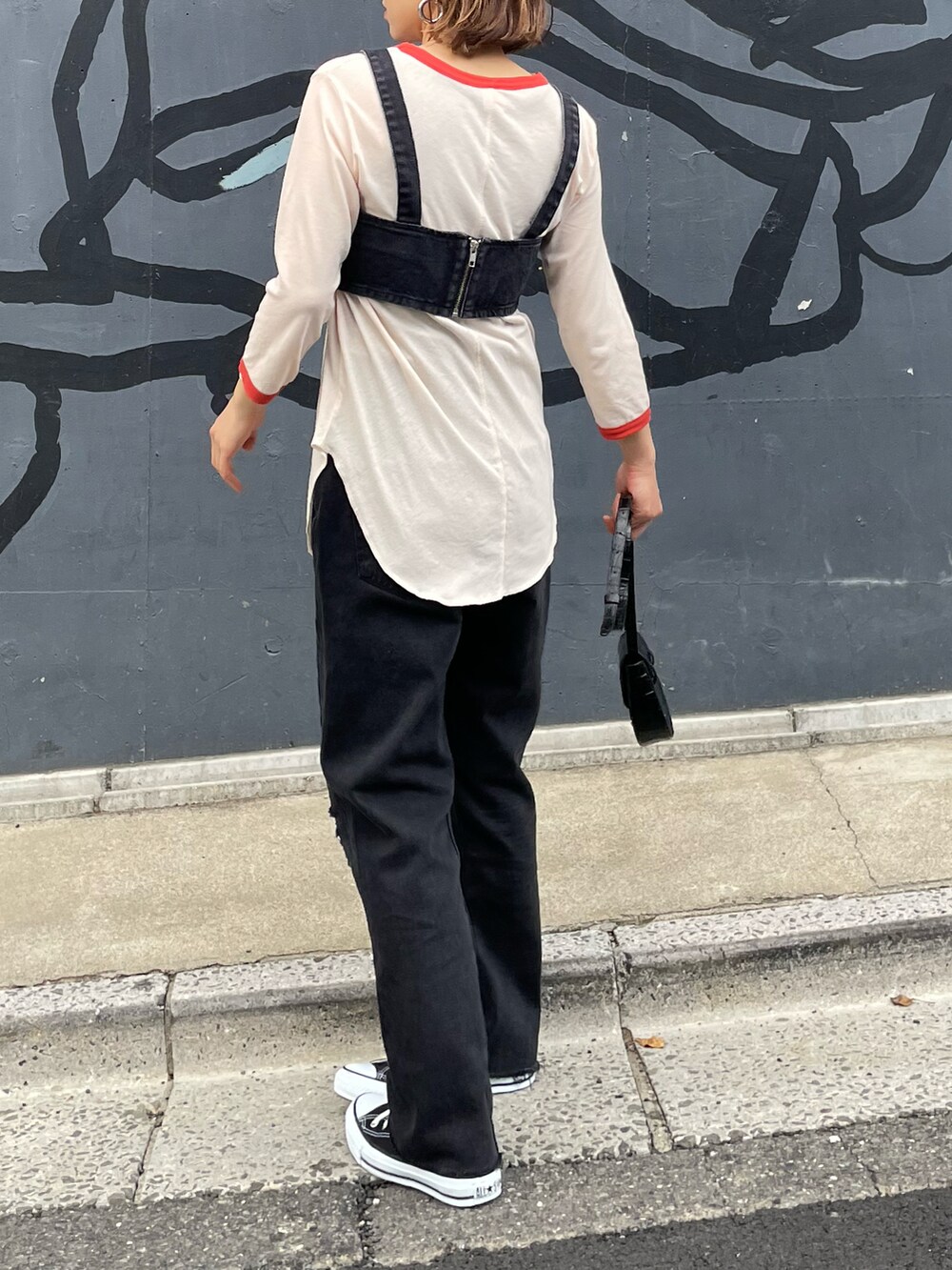 オレンジ系のTシャツ/カットソー、ブラック系のデニムパンツ、ブラック系のスニーカーを着用したレディースの春コーディネートの5枚目の写真