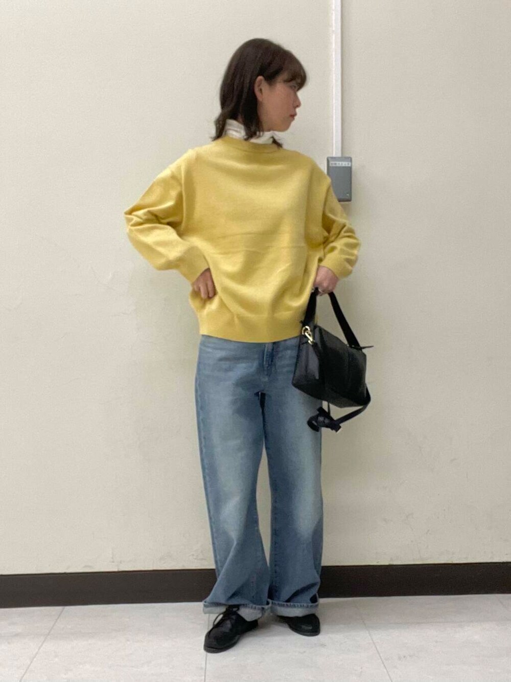 イエロー系のニット/セーター、ブルー系のデニムパンツ、ブラック系のショルダーバッグを着用したレディースの冬コーディネートの2枚目の写真