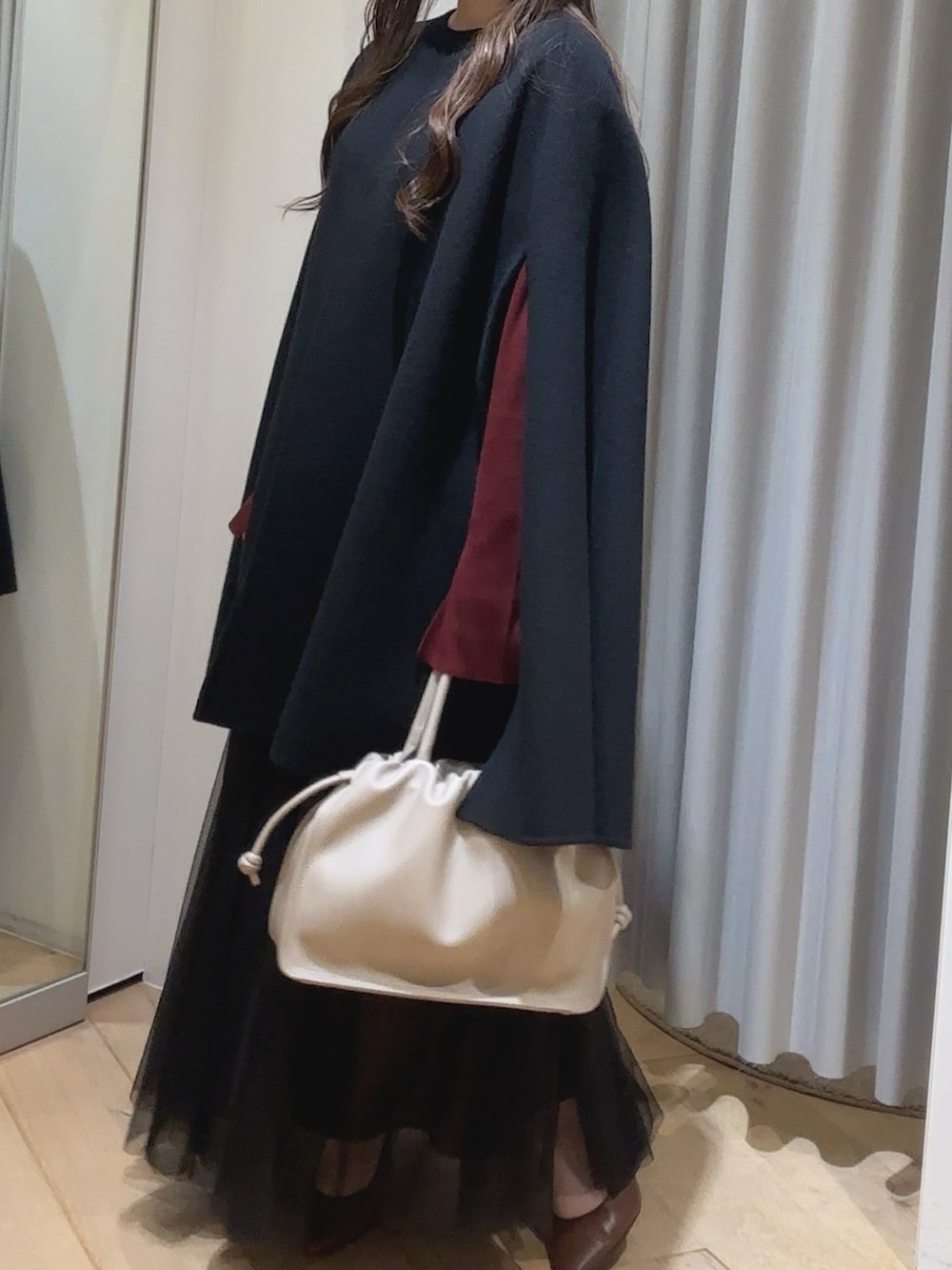 ブルー系のポンチョ、レッド系のニット/セーター、ベージュ系のトートバッグを着用したレディースの秋コーディネートの2枚目の写真