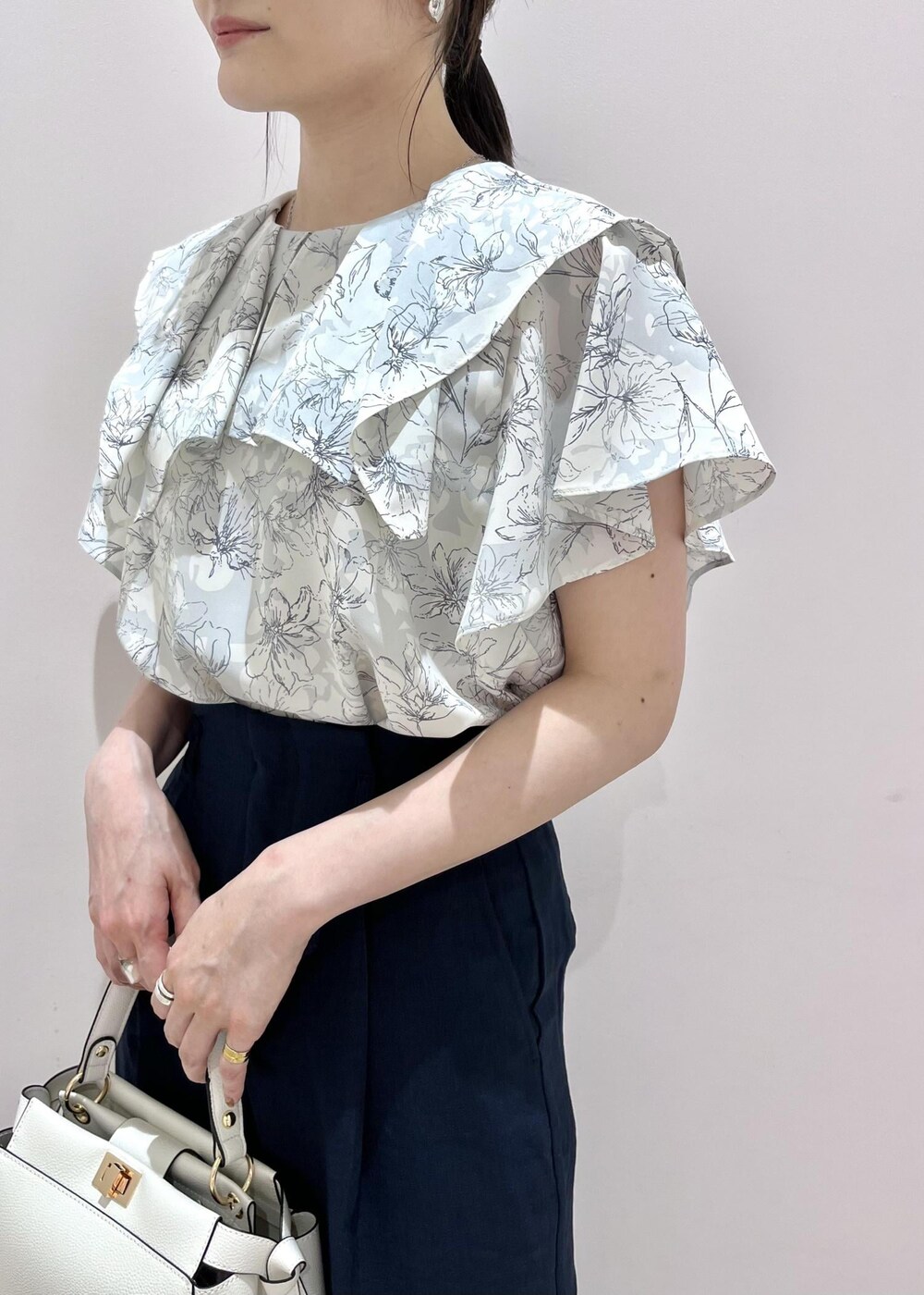 ホワイト系のハンドバッグ、ブルー系のスラックス、シルバー系のサンダルを着用したレディースの春コーディネートの2枚目の写真