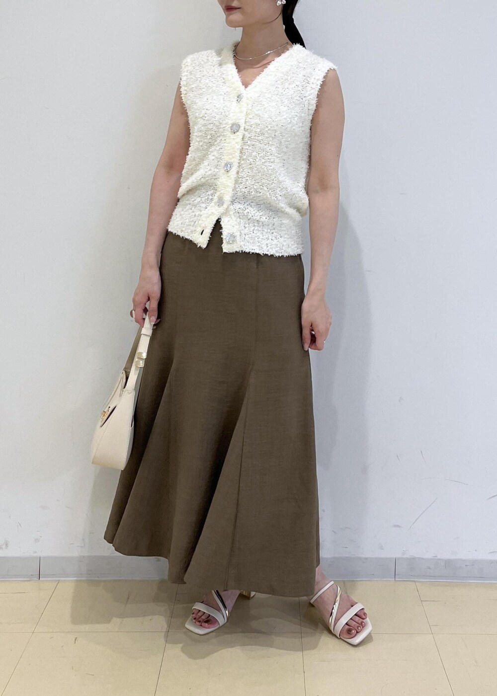 ホワイト系のハンドバッグ、グリーン系のスカート、ホワイト系のサンダルを着用したレディースの春コーディネートの2枚目の写真