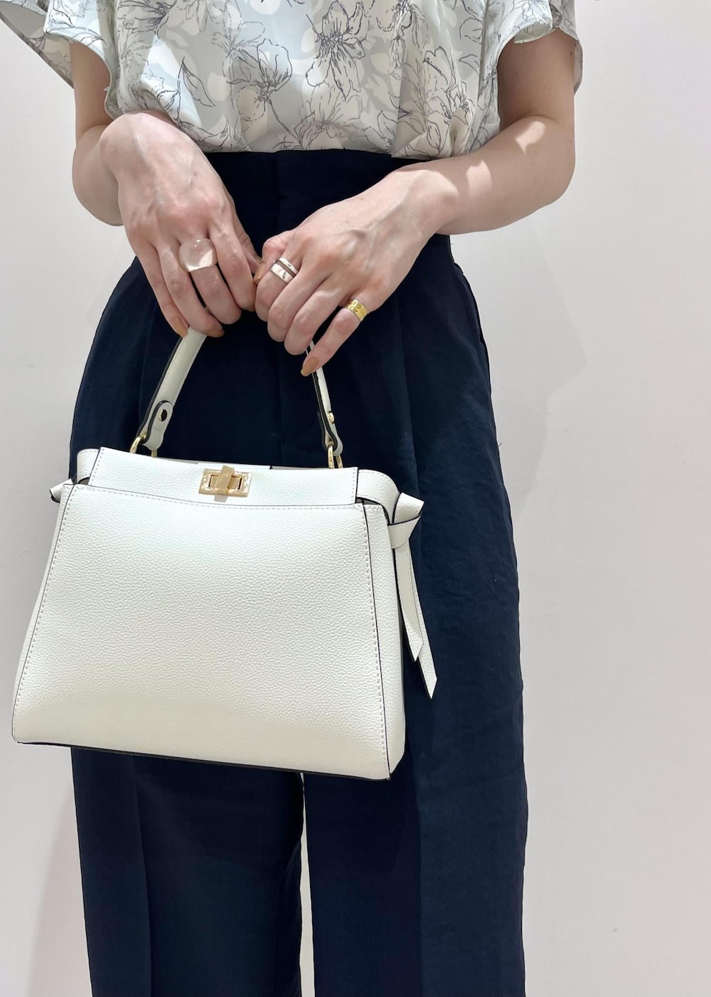 ホワイト系のハンドバッグ、ブルー系のスラックス、シルバー系のサンダルを着用したレディースの春コーディネートの3枚目の写真