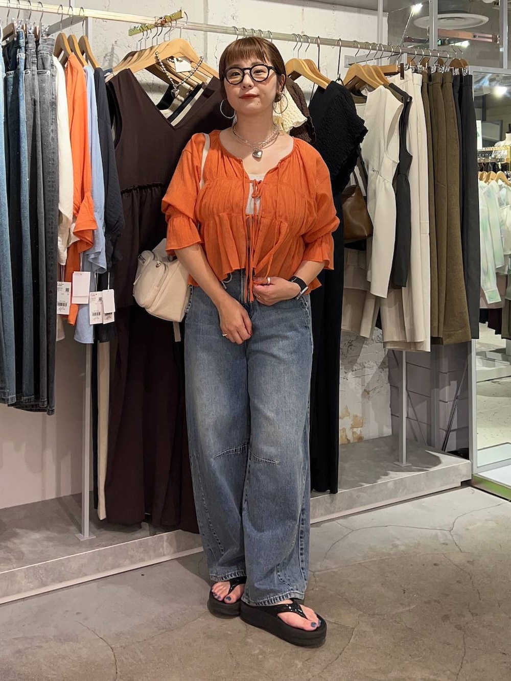 オレンジ系のシャツ/ブラウス、ブルー系のデニムパンツ、ゴールド系のタンクトップを着用したレディースの夏コーディネートの2枚目の写真