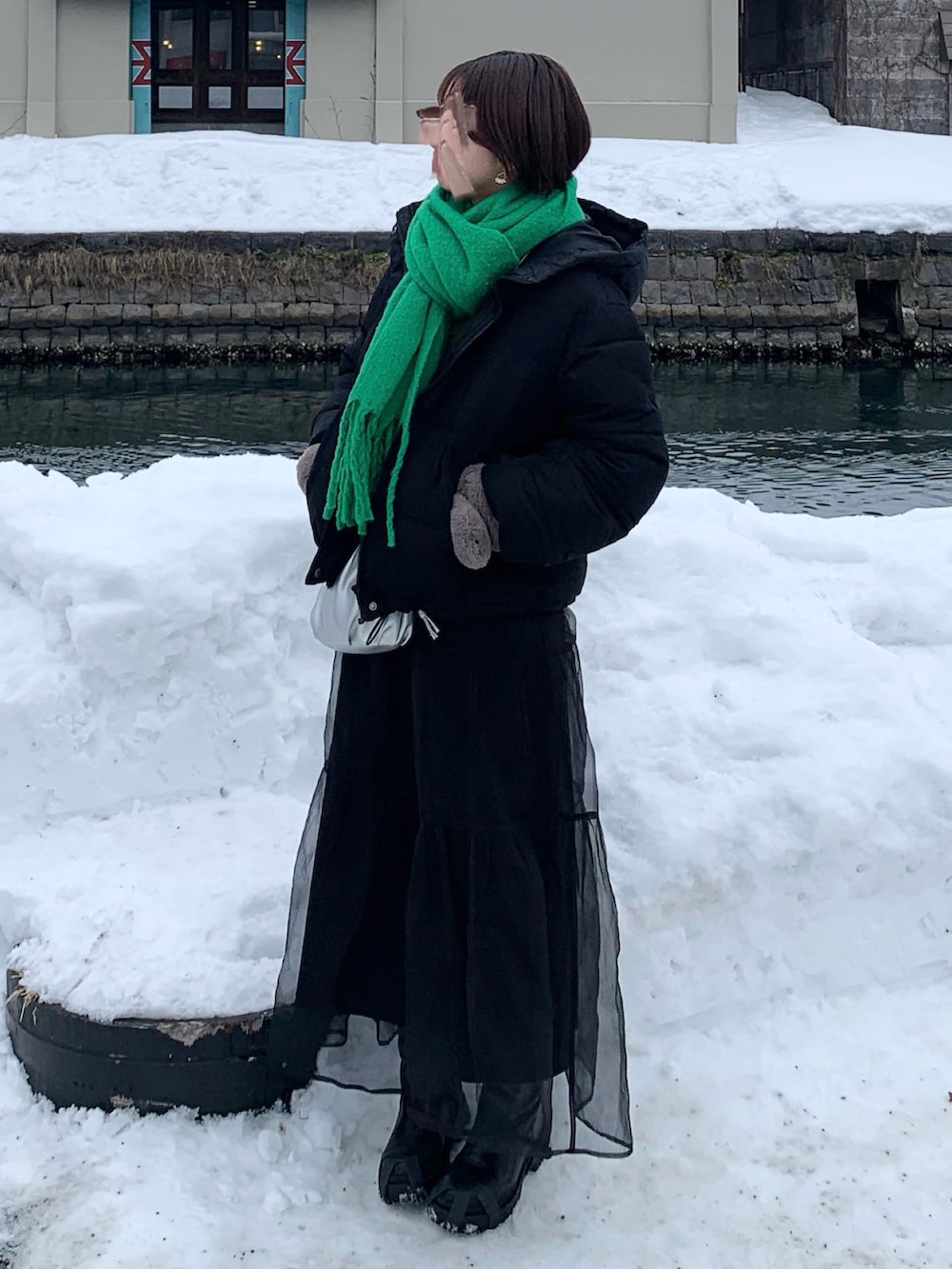 ブラック系のダウンジャケット/コート、ブラック系のスカート、グリーン系のマフラーを着用したレディースの冬コーディネートの2枚目の写真