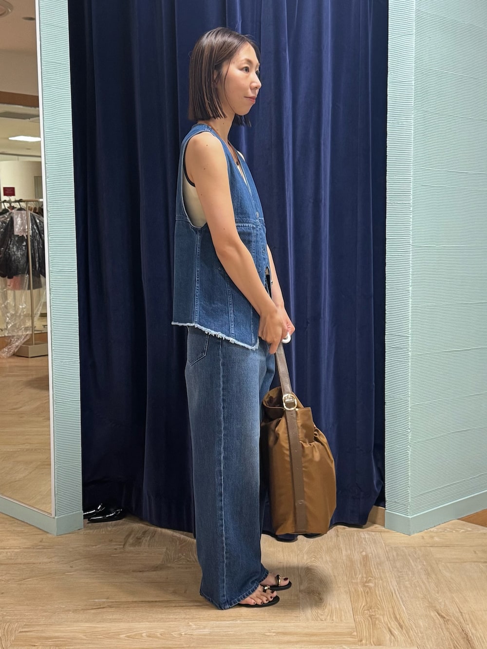 ブルー系のベスト、ブルー系のデニムパンツ、ブラウン系のショルダーバッグを着用したレディースの秋コーディネートの3枚目の写真