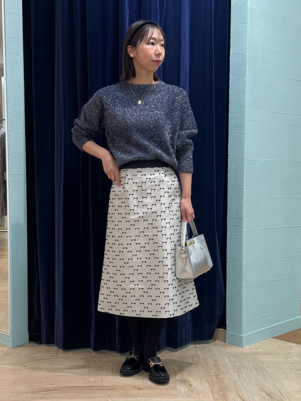 ベージュ系のスカート、ブルー系のニット/セーター、シルバー系のショルダーバッグを着用したレディースの冬コーディネートの2枚目の写真