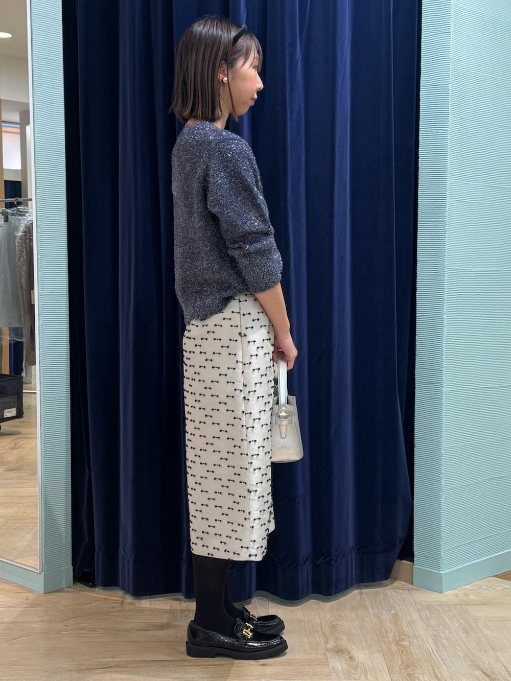 ベージュ系のスカート、ブルー系のニット/セーター、シルバー系のショルダーバッグを着用したレディースの冬コーディネートの3枚目の写真