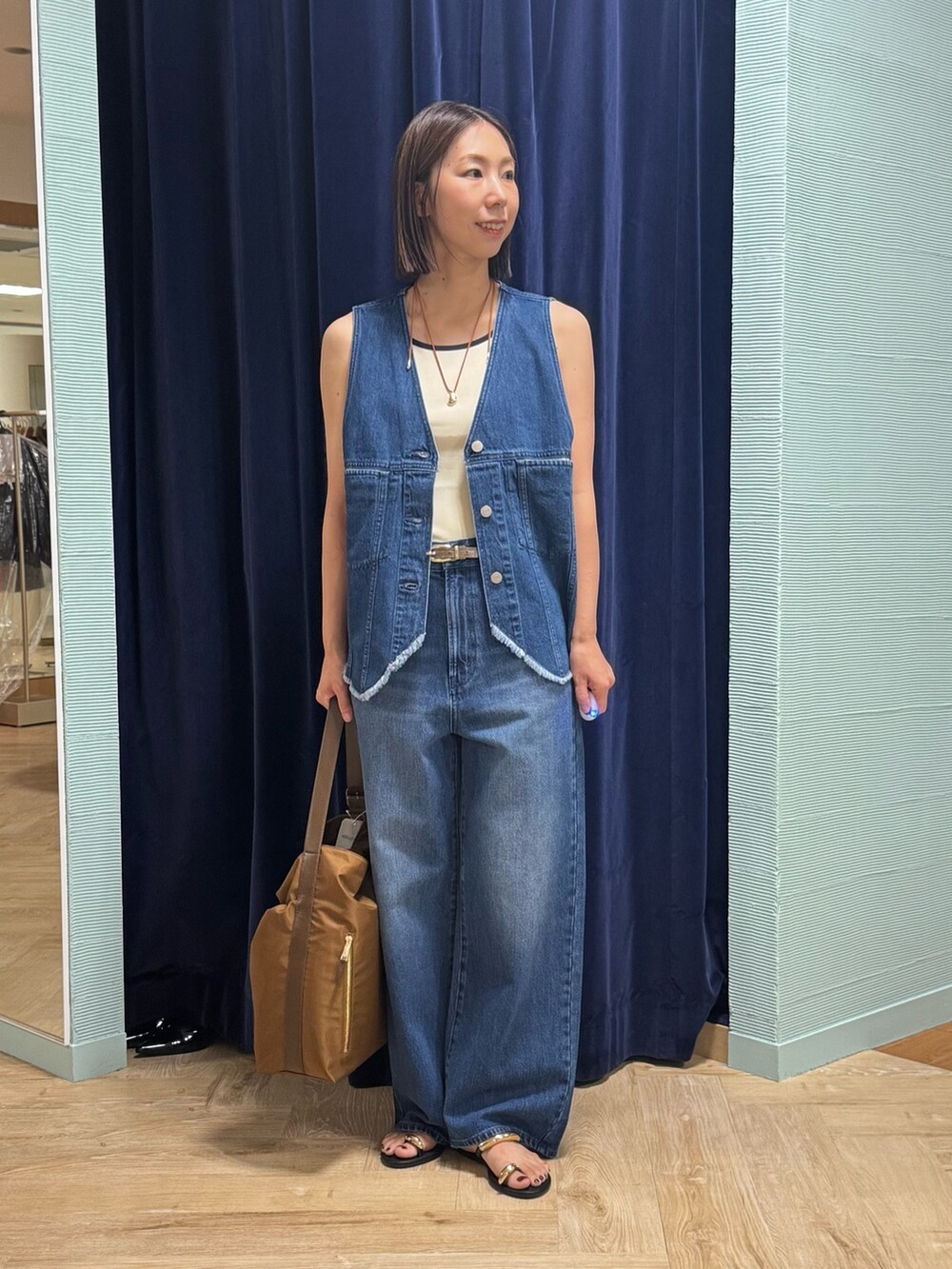 ブルー系のベスト、ブルー系のデニムパンツ、ブラウン系のショルダーバッグを着用したレディースの秋コーディネートの6枚目の写真