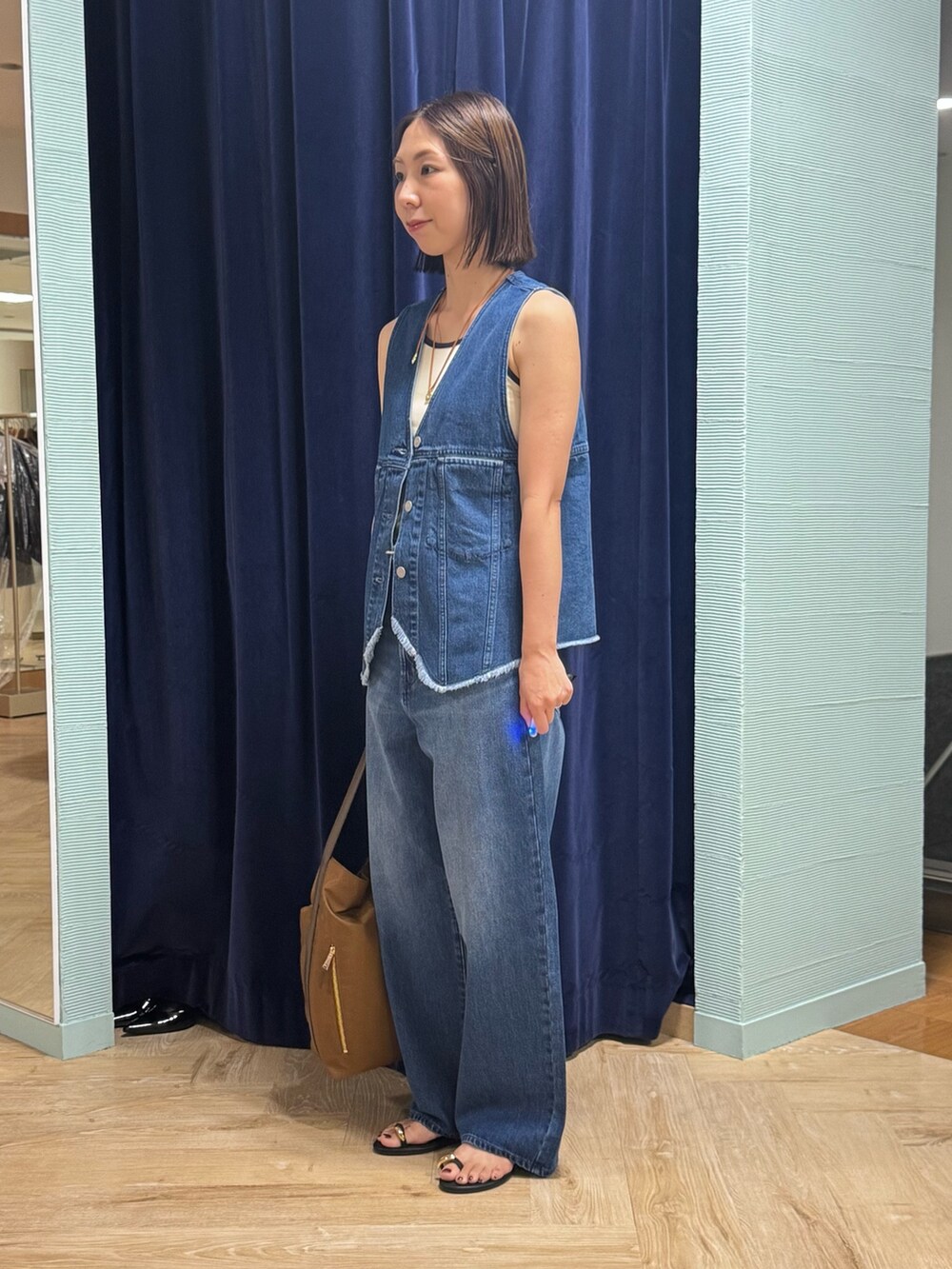 ブルー系のベスト、ブルー系のデニムパンツ、ブラウン系のショルダーバッグを着用したレディースの秋コーディネートの5枚目の写真