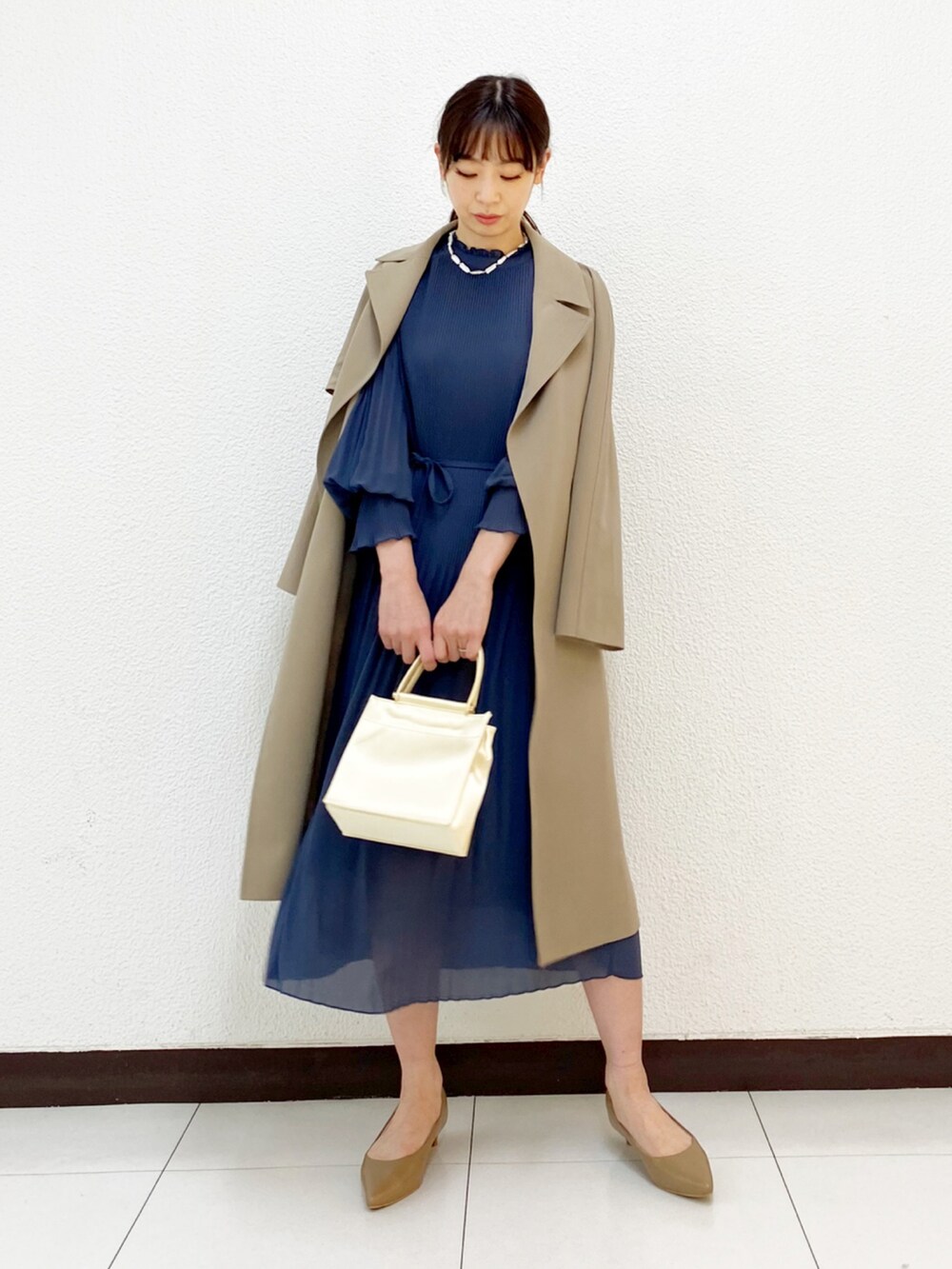ホワイト系のハンドバッグ、ブルー系のワンピース、ベージュ系のトレンチコートを着用したレディースの冬コーディネートの2枚目の写真