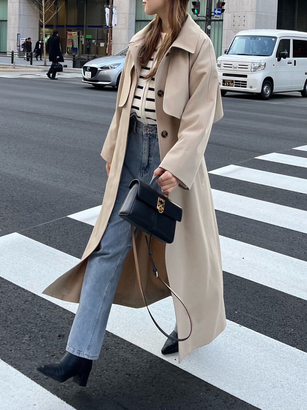 ベージュ系のステンカラーコート、ホワイト系のカーディガン/ボレロ、ブルー系のデニムパンツを着用したレディースの冬コーディネートの2枚目の写真