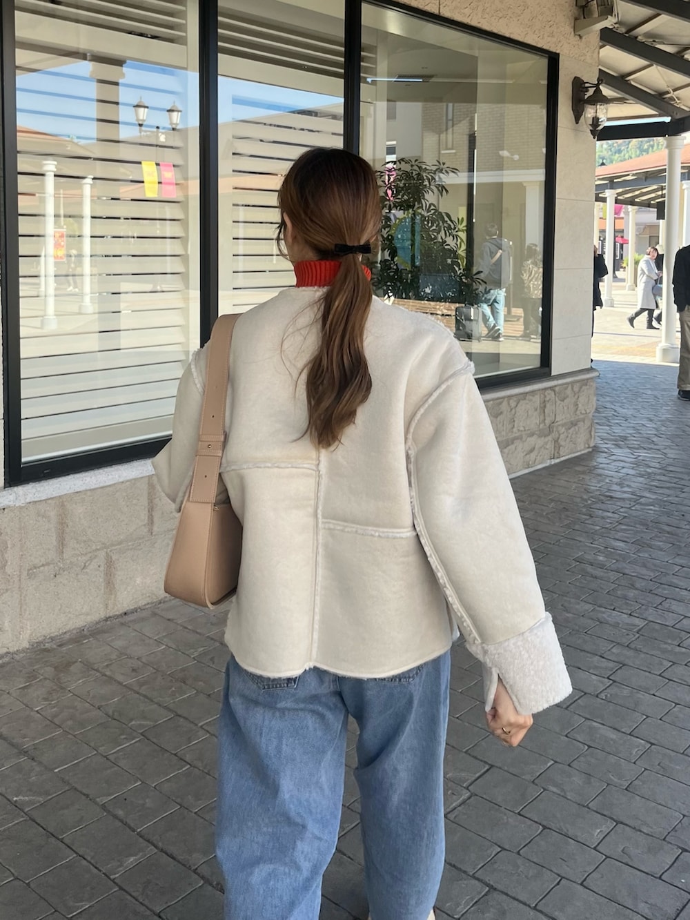 オレンジ系のニット/セーター、ホワイト系のブルゾン、ベージュ系のショルダーバッグを着用したレディースの秋コーディネートの2枚目の写真