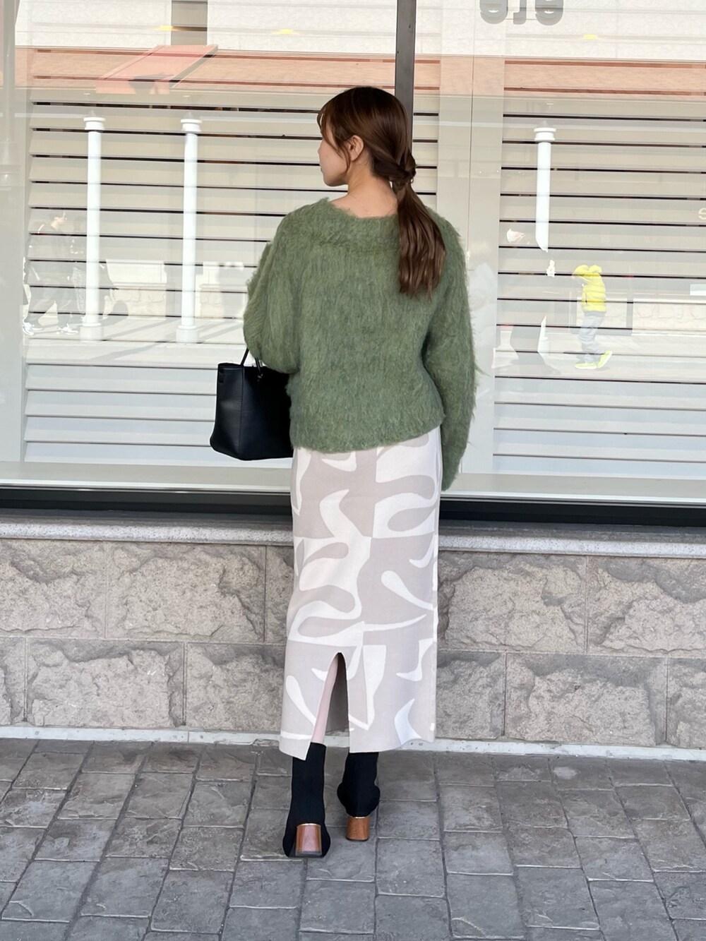 グリーン系のニット/セーター、ベージュ系のスカート、ブラック系のブーツを着用したレディースの冬コーディネートの3枚目の写真
