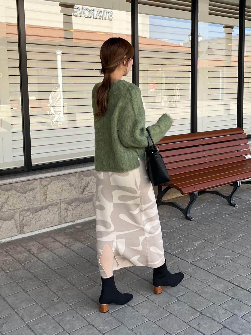 グリーン系のニット/セーター、ベージュ系のスカート、ブラック系のブーツを着用したレディースの冬コーディネートの5枚目の写真