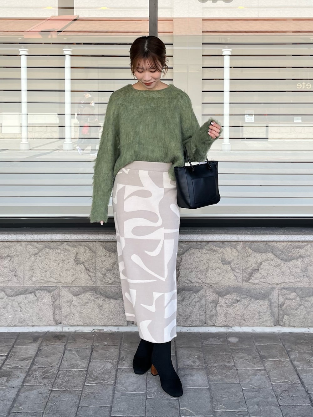 グリーン系のニット/セーター、ベージュ系のスカート、ブラック系のブーツを着用したレディースの冬コーディネートの2枚目の写真