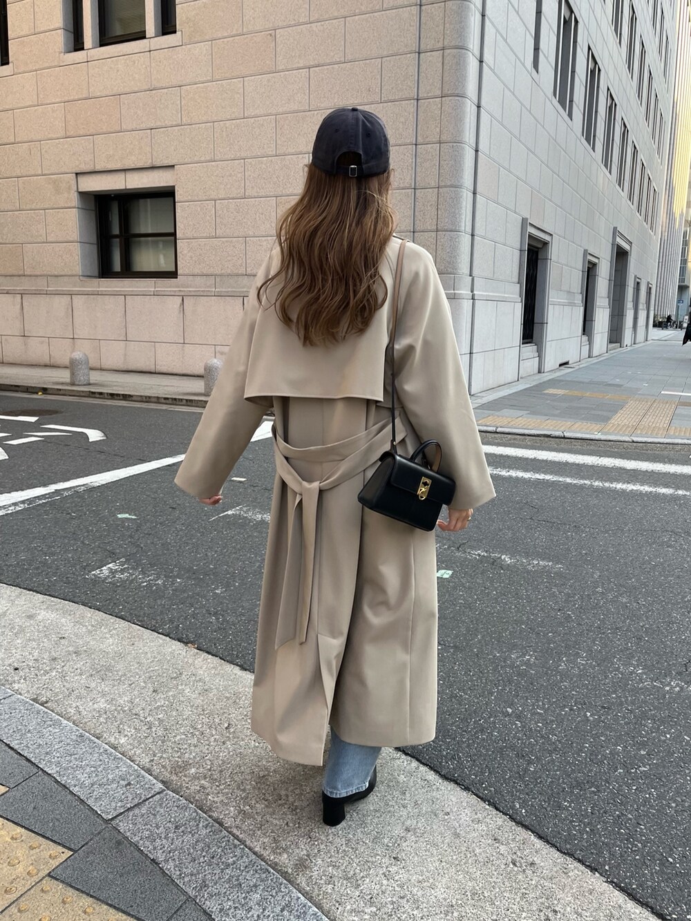 ベージュ系のステンカラーコート、ホワイト系のカーディガン/ボレロ、ブルー系のデニムパンツを着用したレディースの冬コーディネートの6枚目の写真