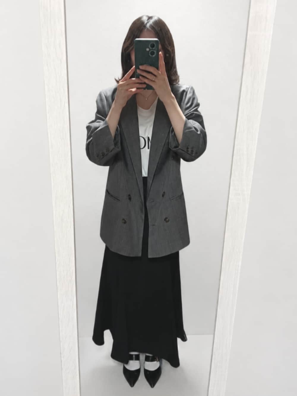 グレー系のテーラードジャケット、ホワイト系のTシャツ/カットソー、ブラック系のスカートを着用したレディースの春コーディネートの2枚目の写真