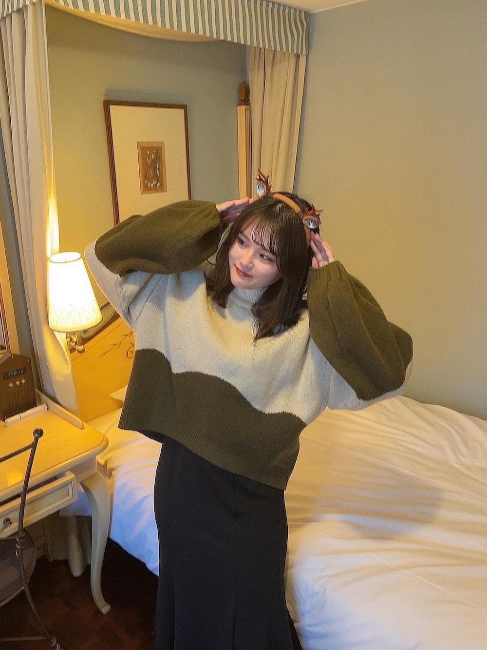 グリーン系のニット/セーター、ブラック系のスカート、ブラック系のブーツを着用したレディースの冬コーディネートの2枚目の写真