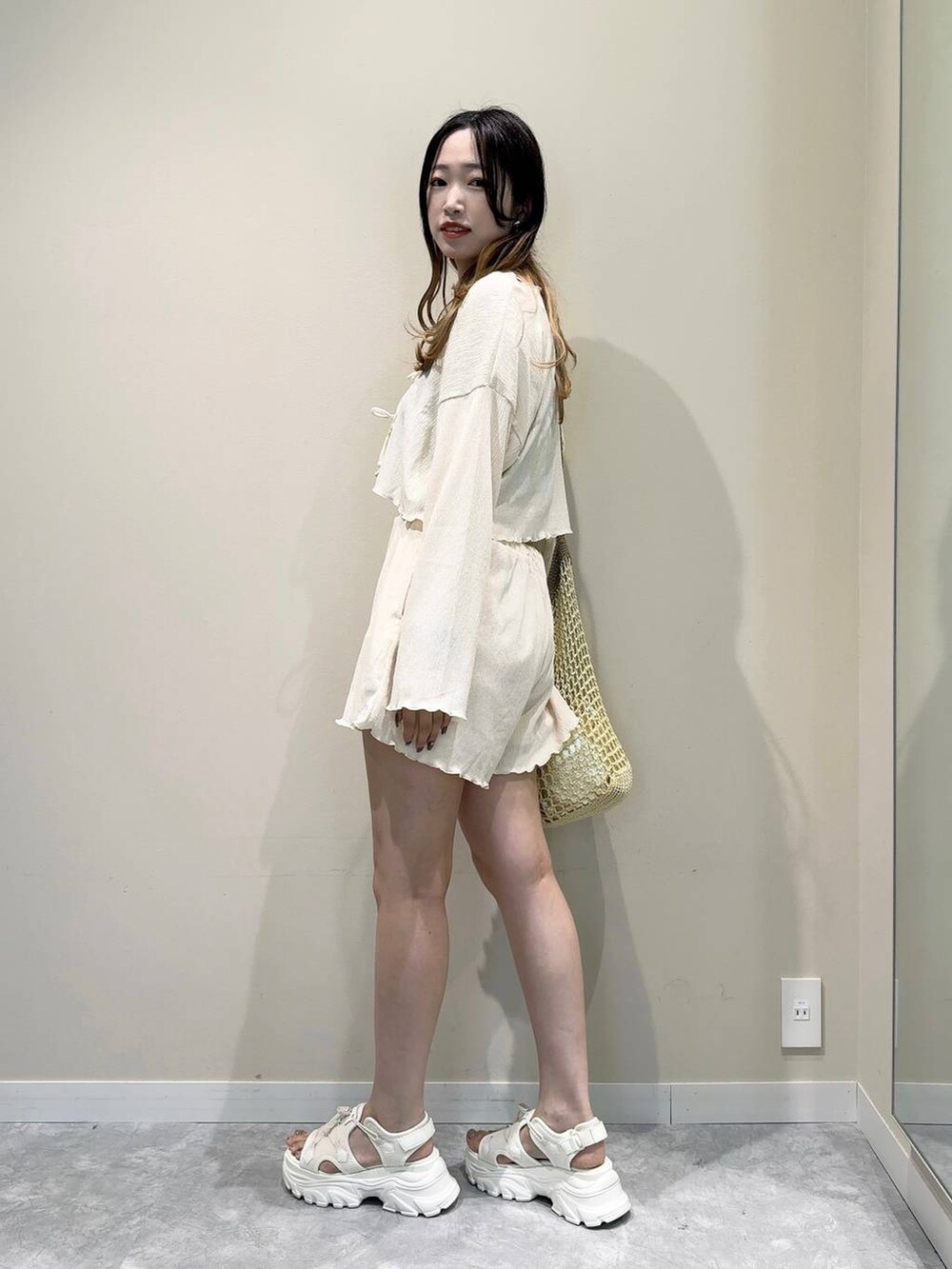 ベージュ系のショルダーバッグ、ホワイト系のサンダル、ベージュ系のラッシュガードを着用したレディースの夏コーディネートの3枚目の写真