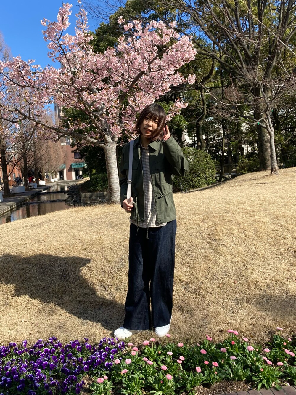 グリーン系のミリタリージャケット、ベージュ系のシャツ/ブラウス、ブルー系のデニムパンツを着用したレディースの春コーディネートの3枚目の写真