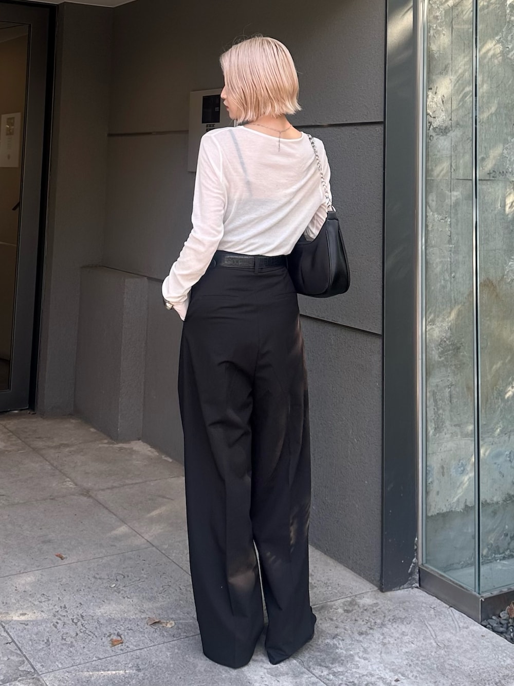 ブラック系のスラックス、ブラック系のショルダーバッグ、ホワイト系のTシャツ/カットソーを着用したレディースの夏コーディネートの4枚目の写真