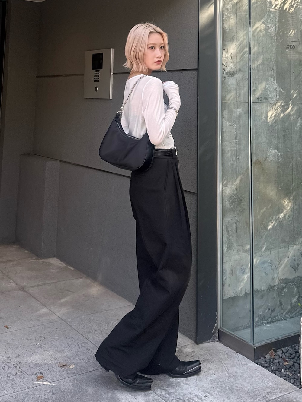 ブラック系のスラックス、ブラック系のショルダーバッグ、ホワイト系のTシャツ/カットソーを着用したレディースの夏コーディネートの3枚目の写真