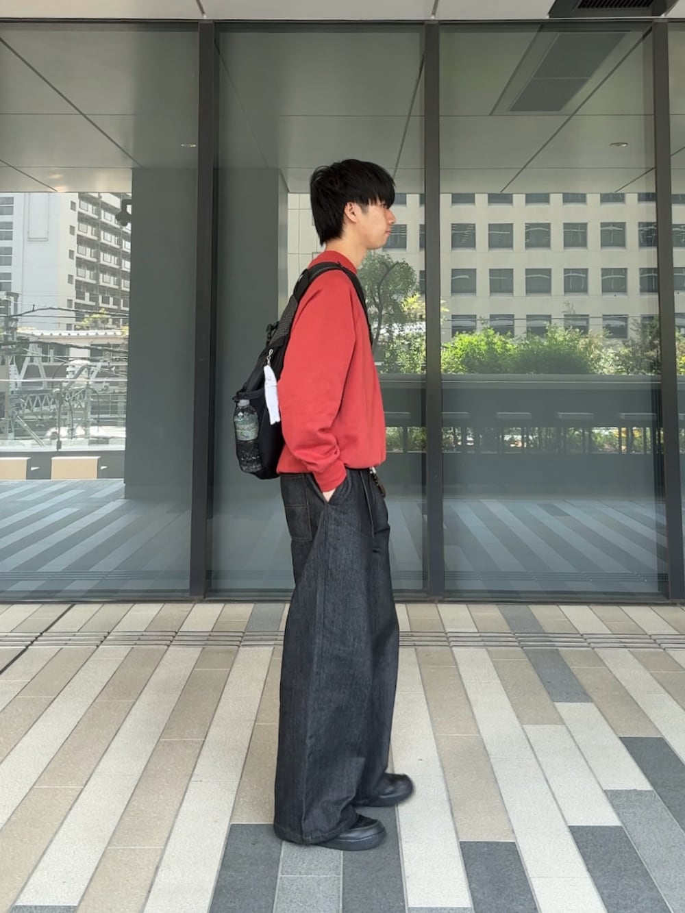 レッド系のスウェット、ブラック系のデニムパンツ、ブラック系のスニーカーを着用したメンズの春コーディネートの2枚目の写真