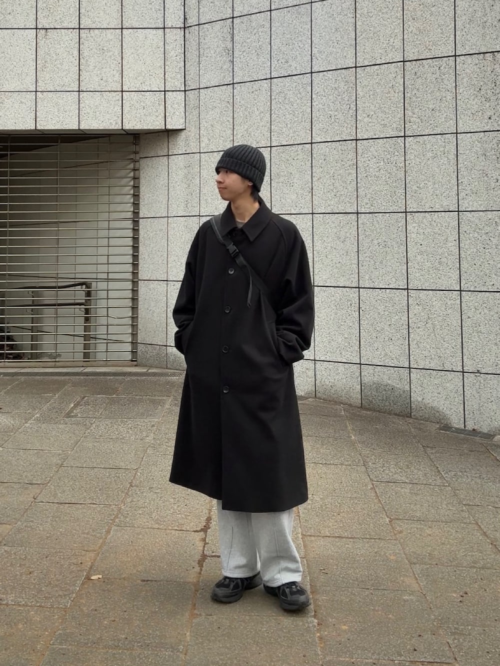 ブラック系のステンカラーコート、グレー系のスウェットパンツ、ブラック系のスニーカーを着用したメンズの冬コーディネートの3枚目の写真