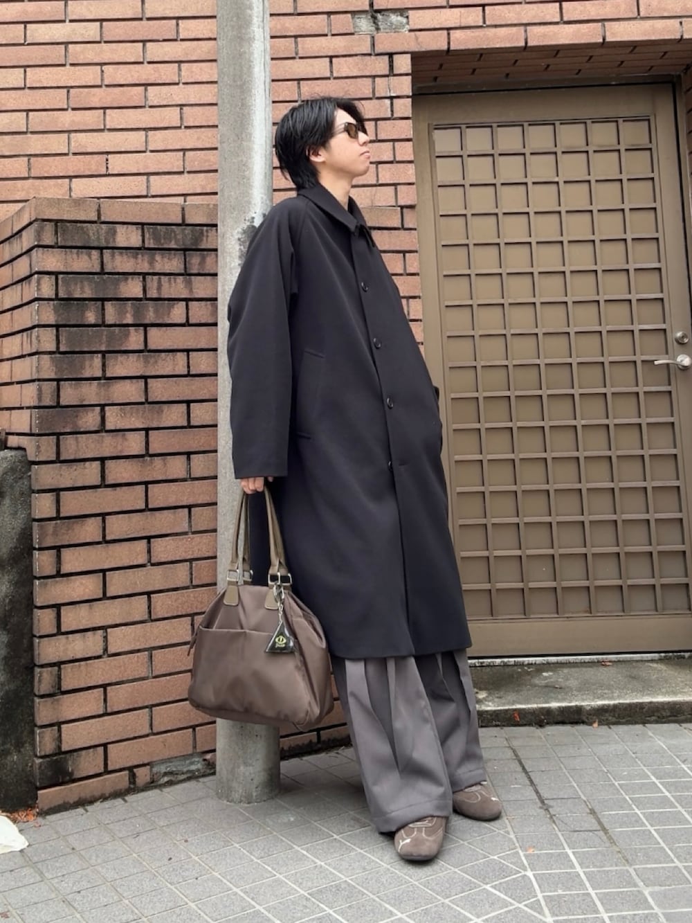 ブラック系のステンカラーコート、グレー系のスラックス、ブラウン系のスニーカーを着用したメンズの春コーディネートの2枚目の写真