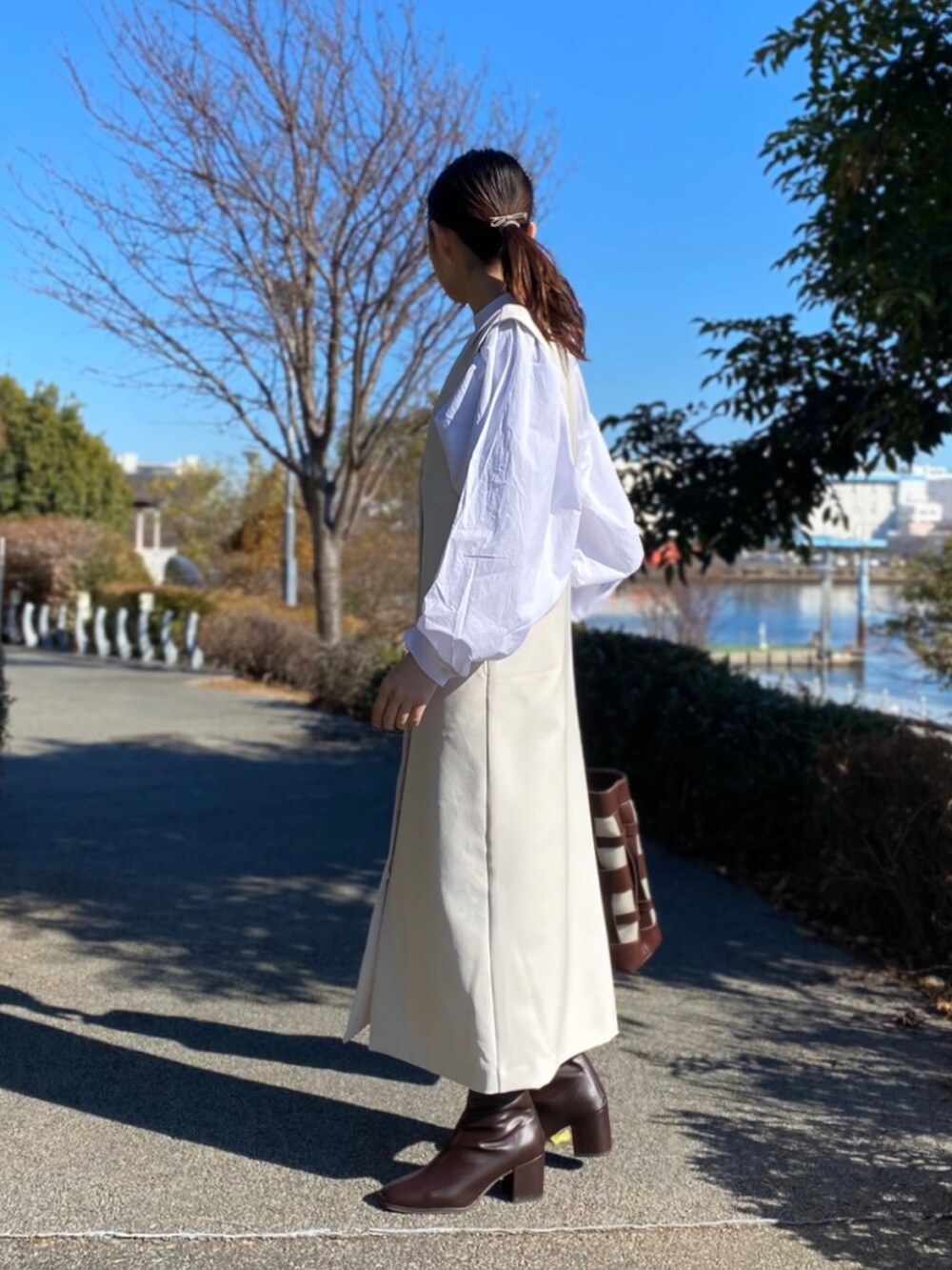 ホワイト系のジャンパースカート、ブラウン系のブーツ、ホワイト系のシャツ/ブラウスを着用したレディースの冬コーディネートの3枚目の写真