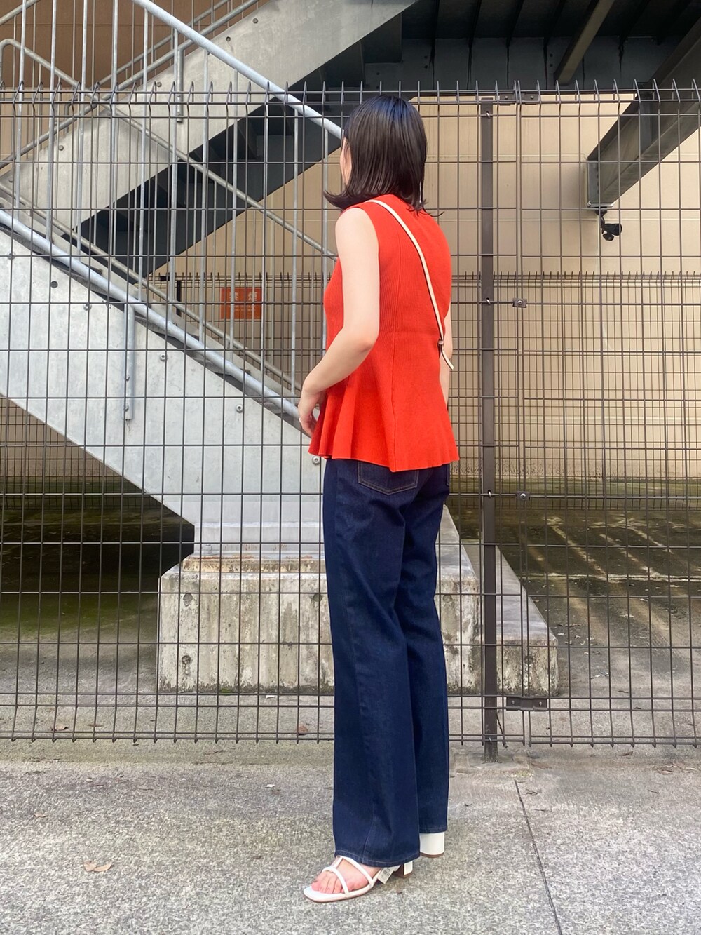 レッド系のニット/セーター、ブルー系のデニムパンツ、ホワイト系のショルダーバッグを着用したレディースの夏コーディネートの2枚目の写真