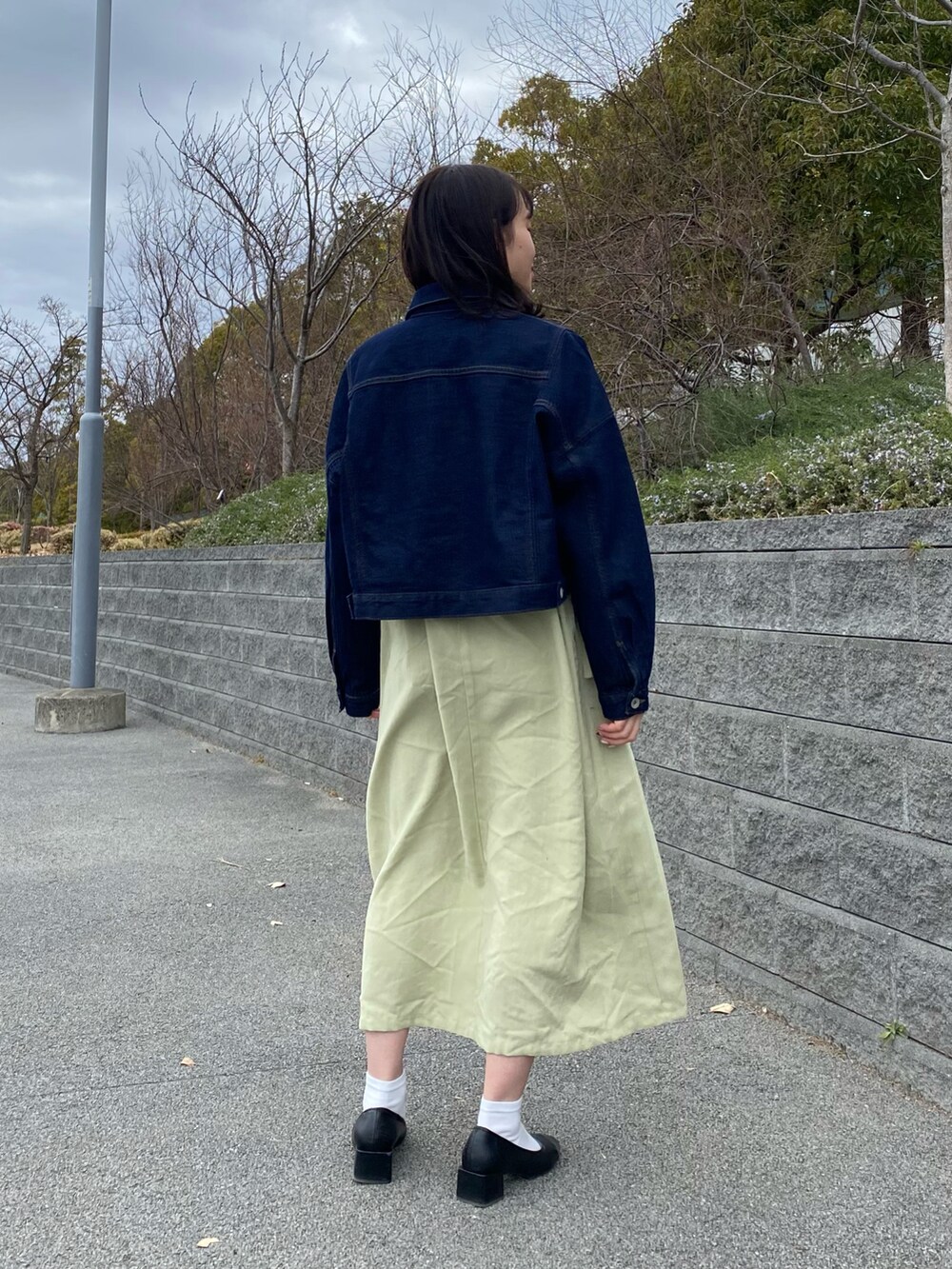 ブルー系のデニムジャケット、グリーン系のワンピース、ブラック系のパンプスを着用したレディースの春コーディネートの3枚目の写真