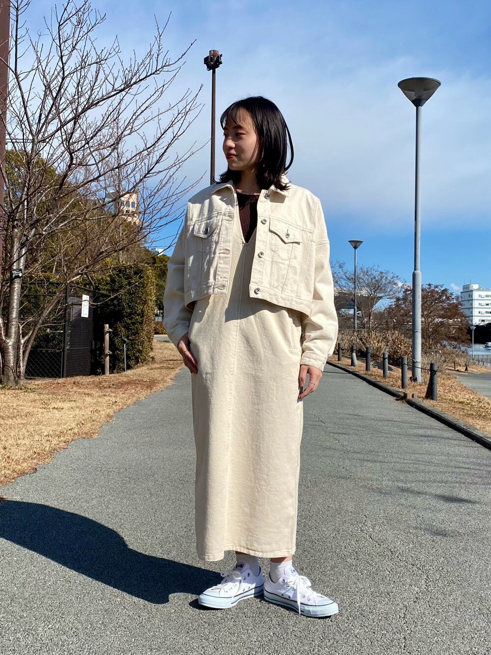 ホワイト系のデニムジャケット、ホワイト系のジャンパースカート、ホワイト系のスニーカーを着用したレディースの冬コーディネートの2枚目の写真