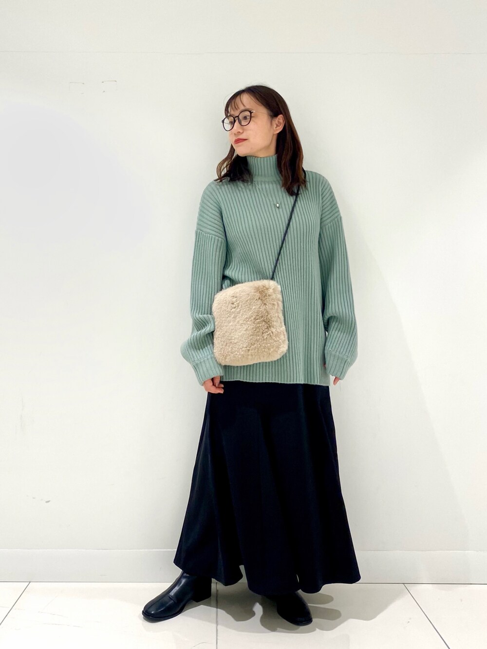 グリーン系のニット/セーター、ブラック系のスカート、ベージュ系のショルダーバッグを着用したレディースの冬コーディネートの2枚目の写真
