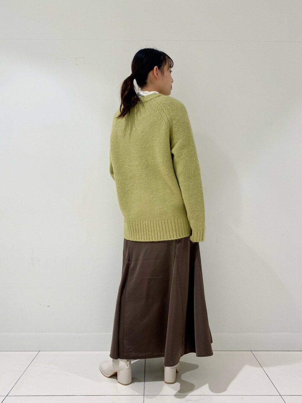 グリーン系のニット/セーター、ブラウン系のスカート、ホワイト系のブーツを着用したレディースの冬コーディネートの3枚目の写真