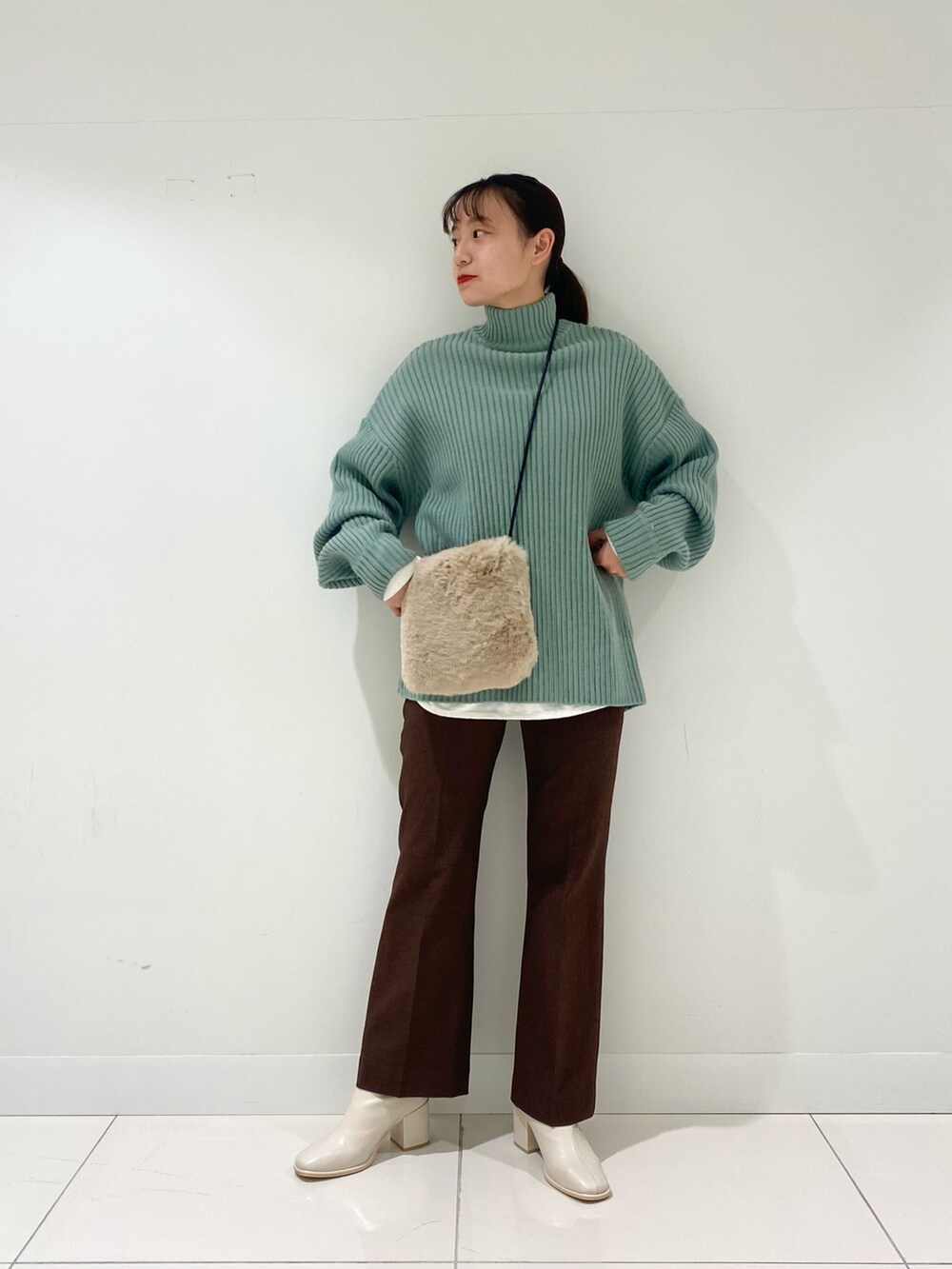 グリーン系のニット/セーター、ホワイト系のTシャツ/カットソー、ホワイト系のブーツを着用したレディースの冬コーディネートの2枚目の写真