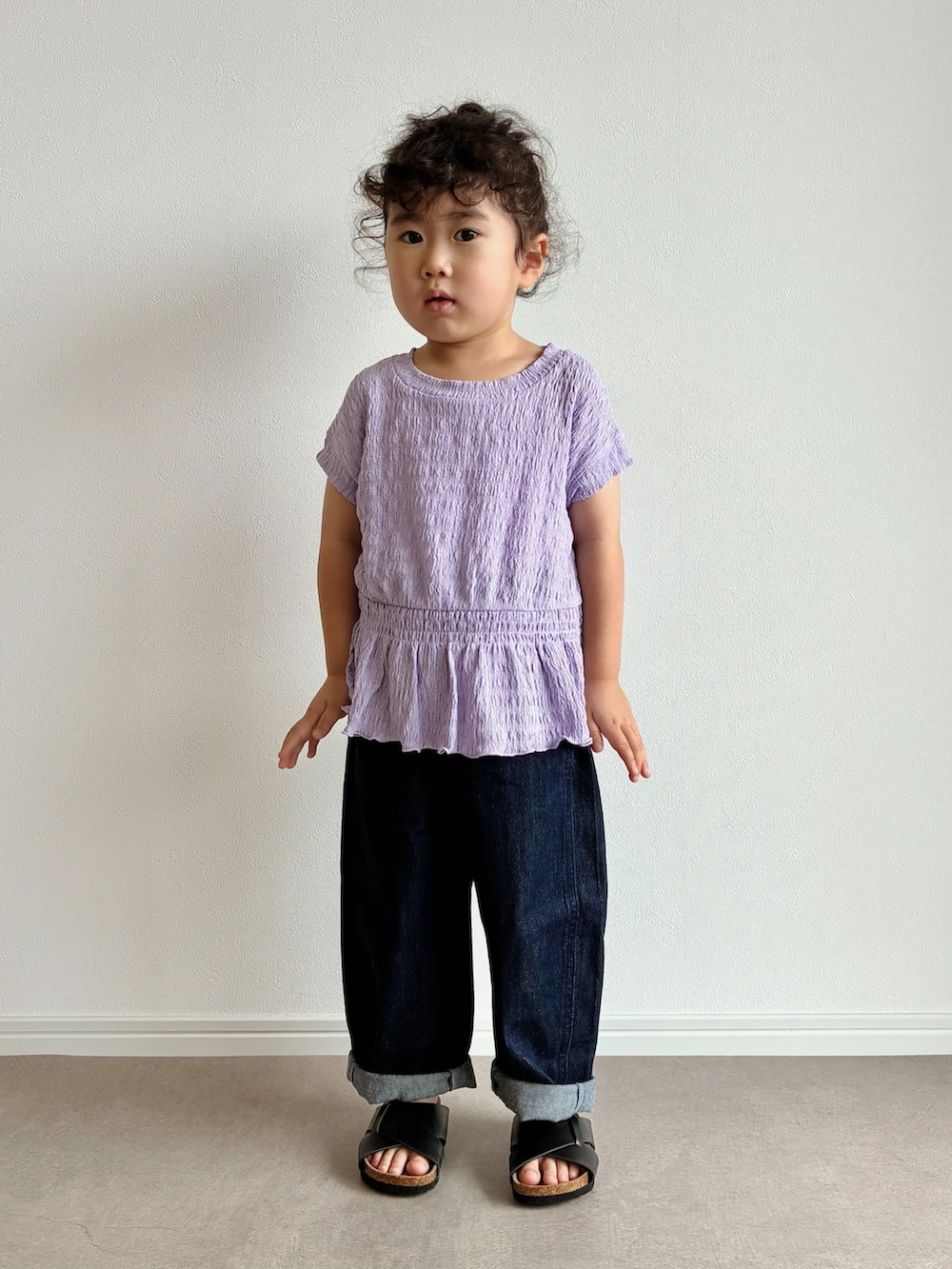 パープル系のトップス、ブルー系のデニムパンツ、ブラック系のサンダルを着用したキッズの夏コーディネートの2枚目の写真