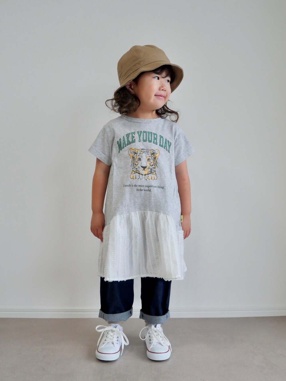 グレー系のワンピース、ブルー系のデニムパンツ、ホワイト系のスニーカーを着用したキッズの秋コーディネートの2枚目の写真