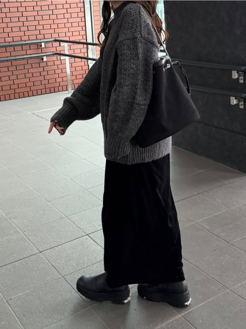 グレー系のニット/セーター、ブラウン系のバッグ、ブラック系のスカートを着用したレディースの冬コーディネートの2枚目の写真