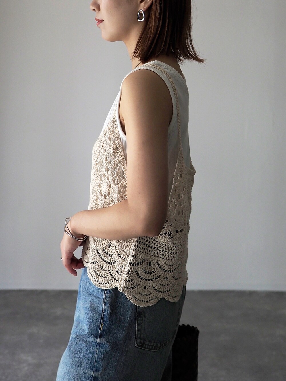 ブラウン系のかごバッグ、ブラック系のサンダル、ホワイト系のベストを着用したレディースの夏コーディネートの4枚目の写真