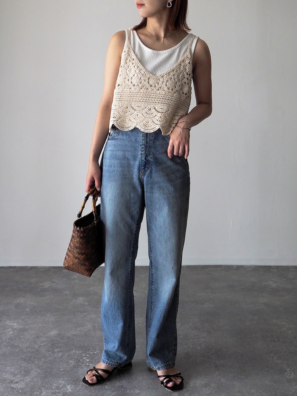 ブラウン系のかごバッグ、ブラック系のサンダル、ホワイト系のベストを着用したレディースの夏コーディネートの2枚目の写真