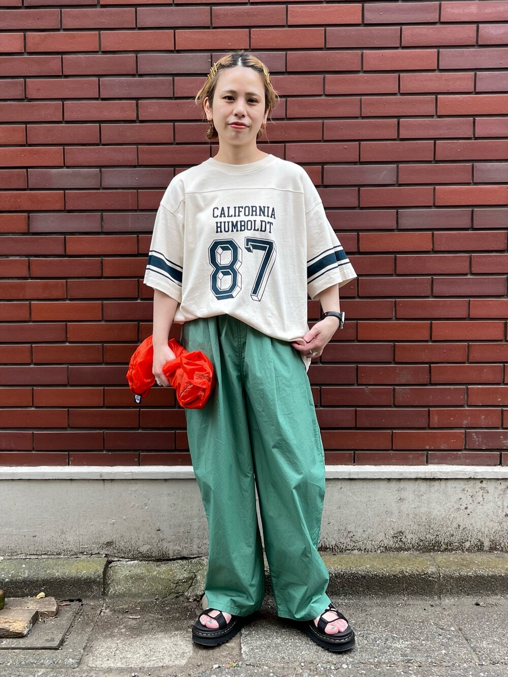 ベージュ系のTシャツ/カットソー、オレンジ系のエコバッグ/サブバッグ、ブラック系のサンダルを着用したレディースの夏コーディネートの2枚目の写真