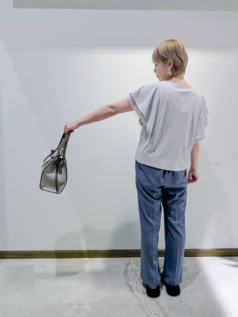 ホワイト系のショルダーバッグ、グレー系のTシャツ/カットソー、ブルー系のスラックスを着用したレディースの秋コーディネートの3枚目の写真