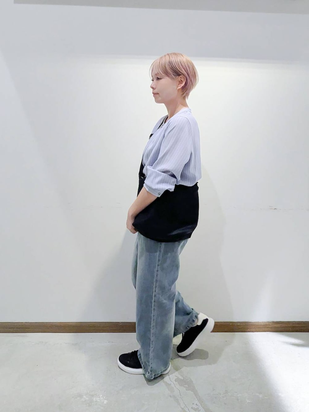 ブラック系のスニーカー、ブラック系のショルダーバッグ、ブルー系のデニムパンツを着用したレディースの秋コーディネートの4枚目の写真