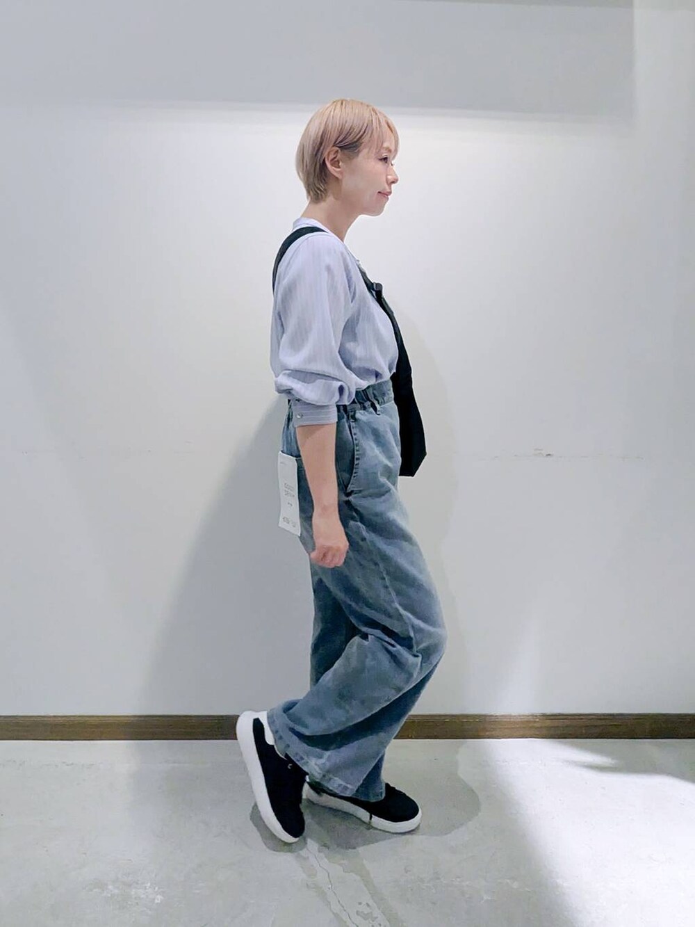 ブラック系のスニーカー、ブラック系のショルダーバッグ、ブルー系のデニムパンツを着用したレディースの秋コーディネートの2枚目の写真